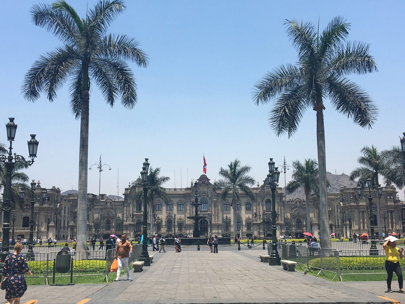 Central Lima scene with palms bordering a large open public square with a large stone palace building filling one end of the square