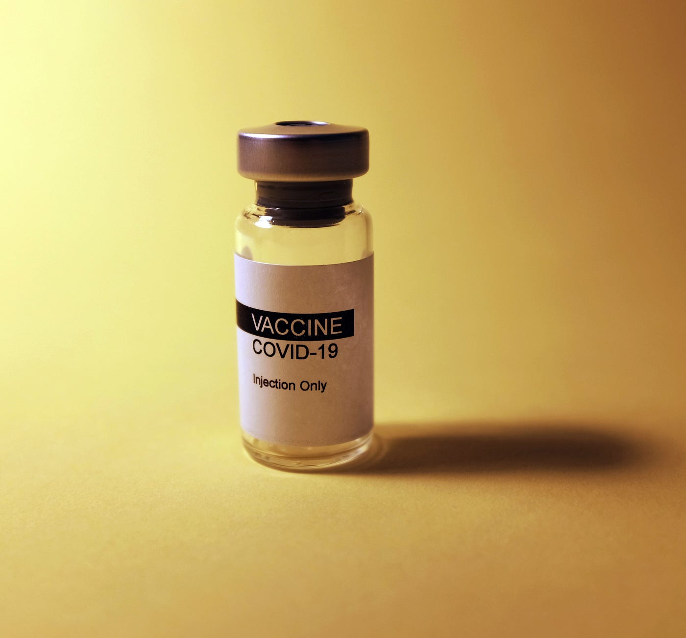 Picture of a COVID-19 vaccine bottle against a yellow background.