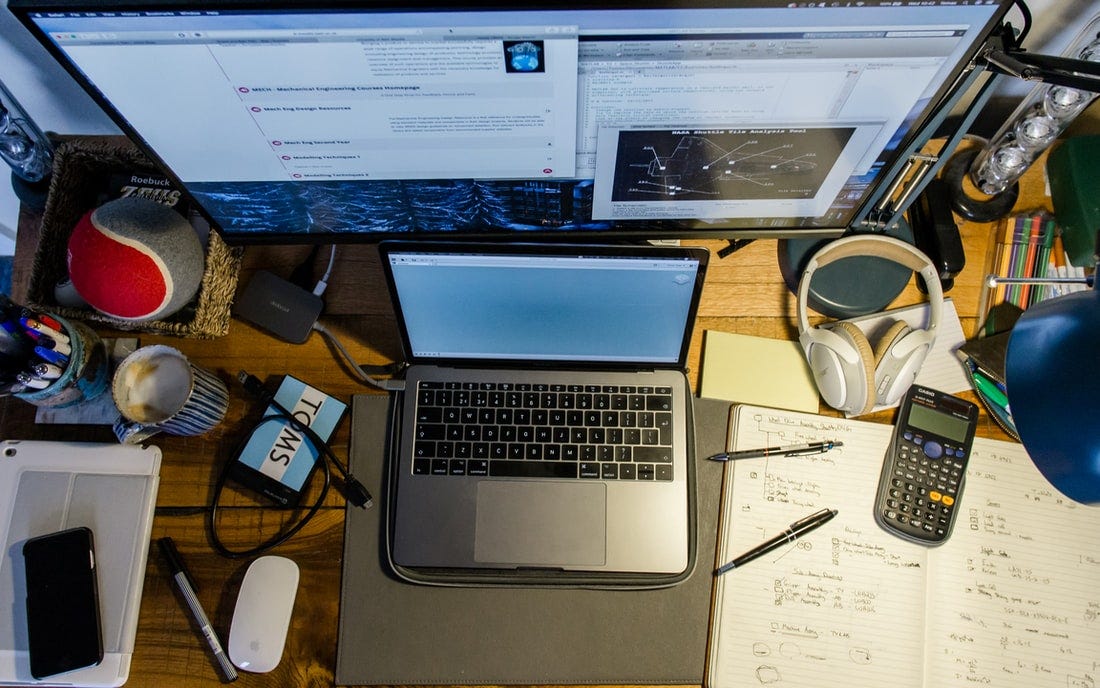 A cluttered desk with headphones, a laptop, a calculator, and other things. The photo is taken from a high angle.
