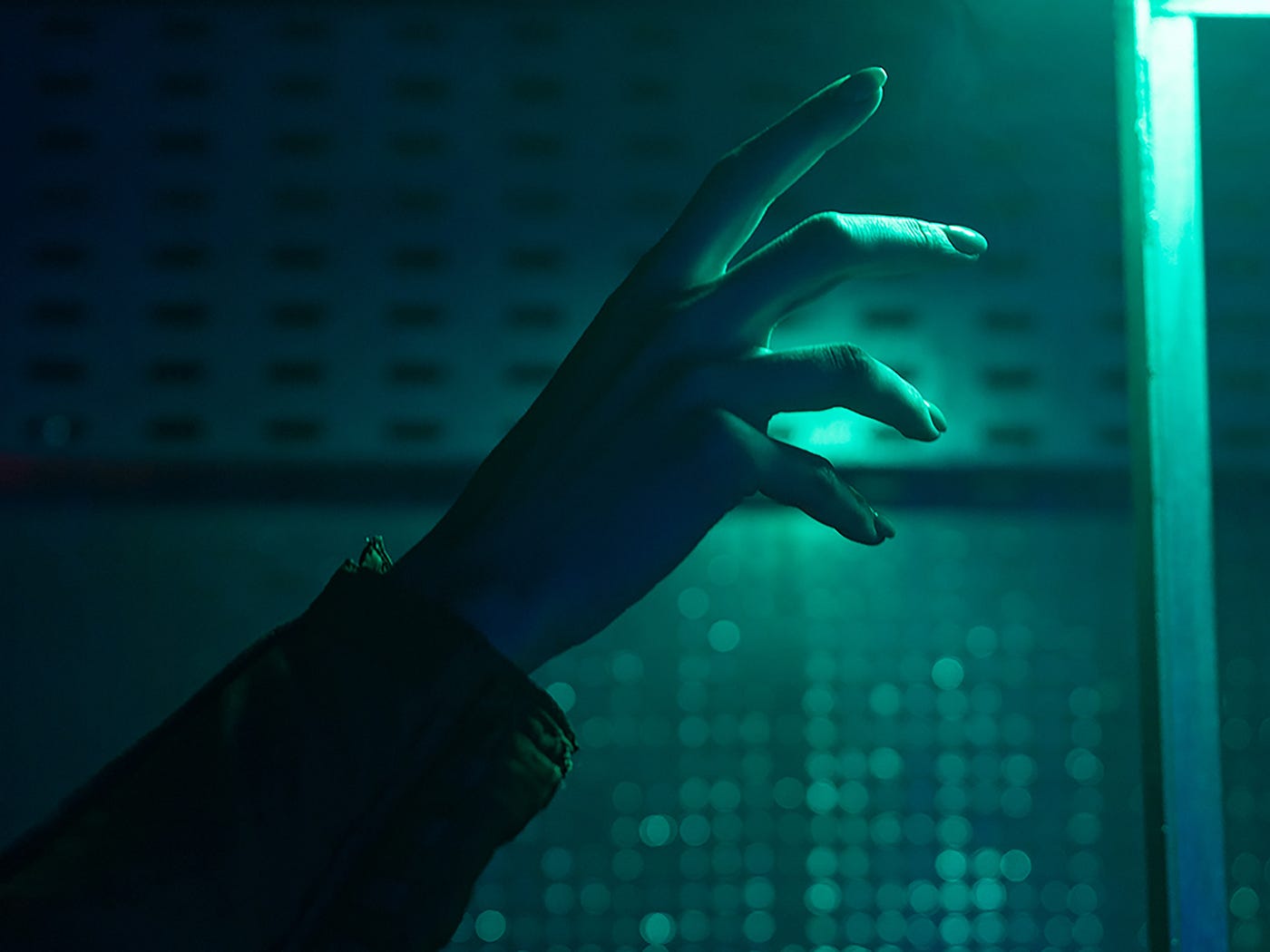 Hand reaches towards a green tinted light in an industrial, high tech background