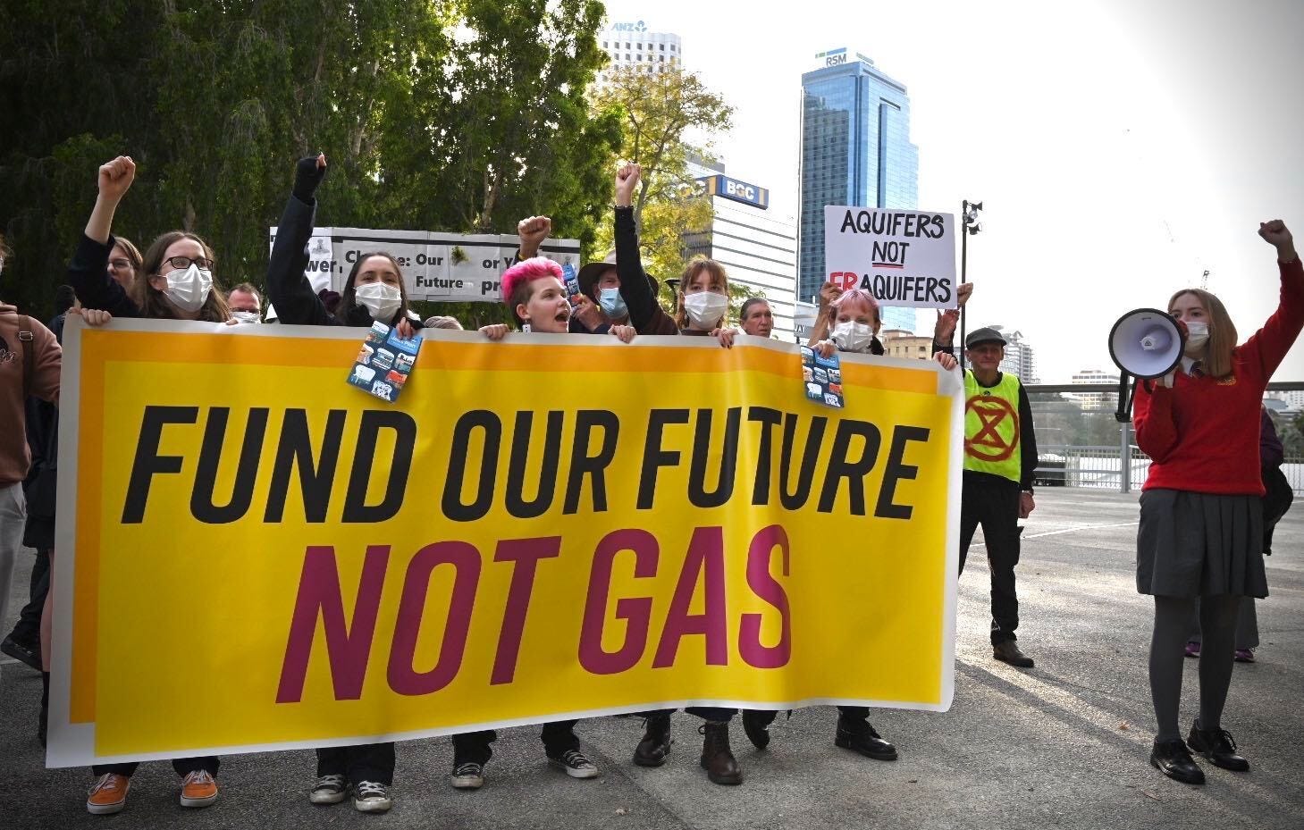 5 students holding a yellow banner that reads: Fund our future, Not gas. Also a student to right holding a megaphone.