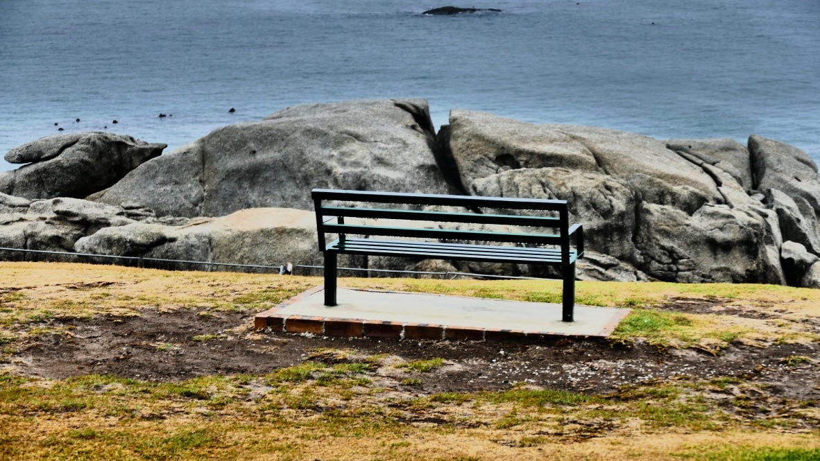 Empty bench overlooking the ocean, with large rocks in front of it.