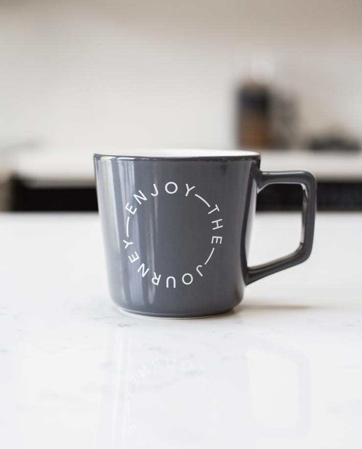 A grey mug with the print “Enjoy the journey”, produced and sold by Ugmonk