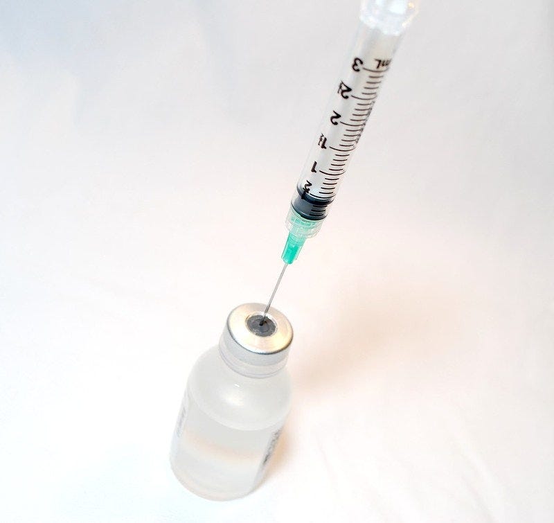 syringe being inserted into medication vial