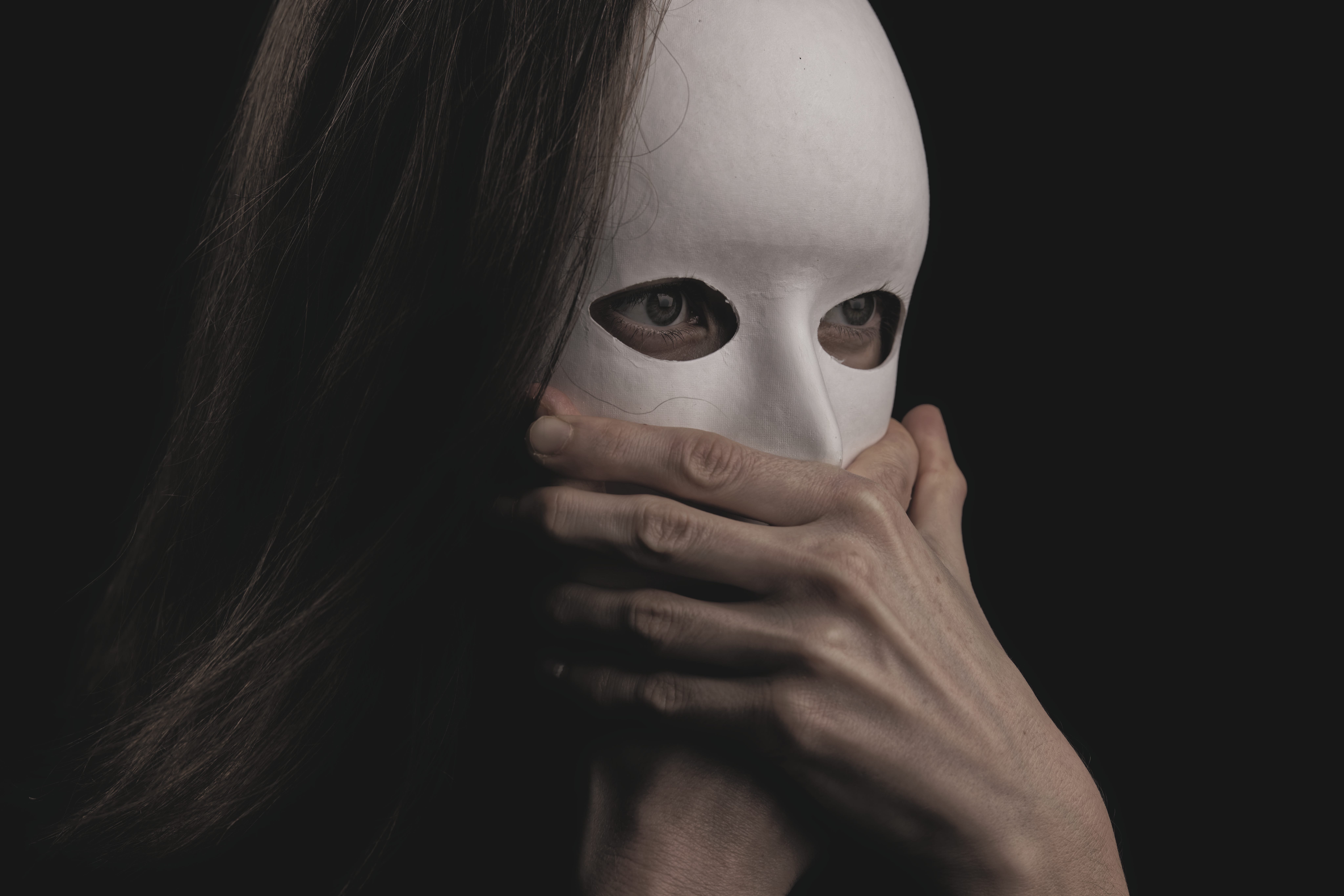 Woman with white mask on, holding her mouth.