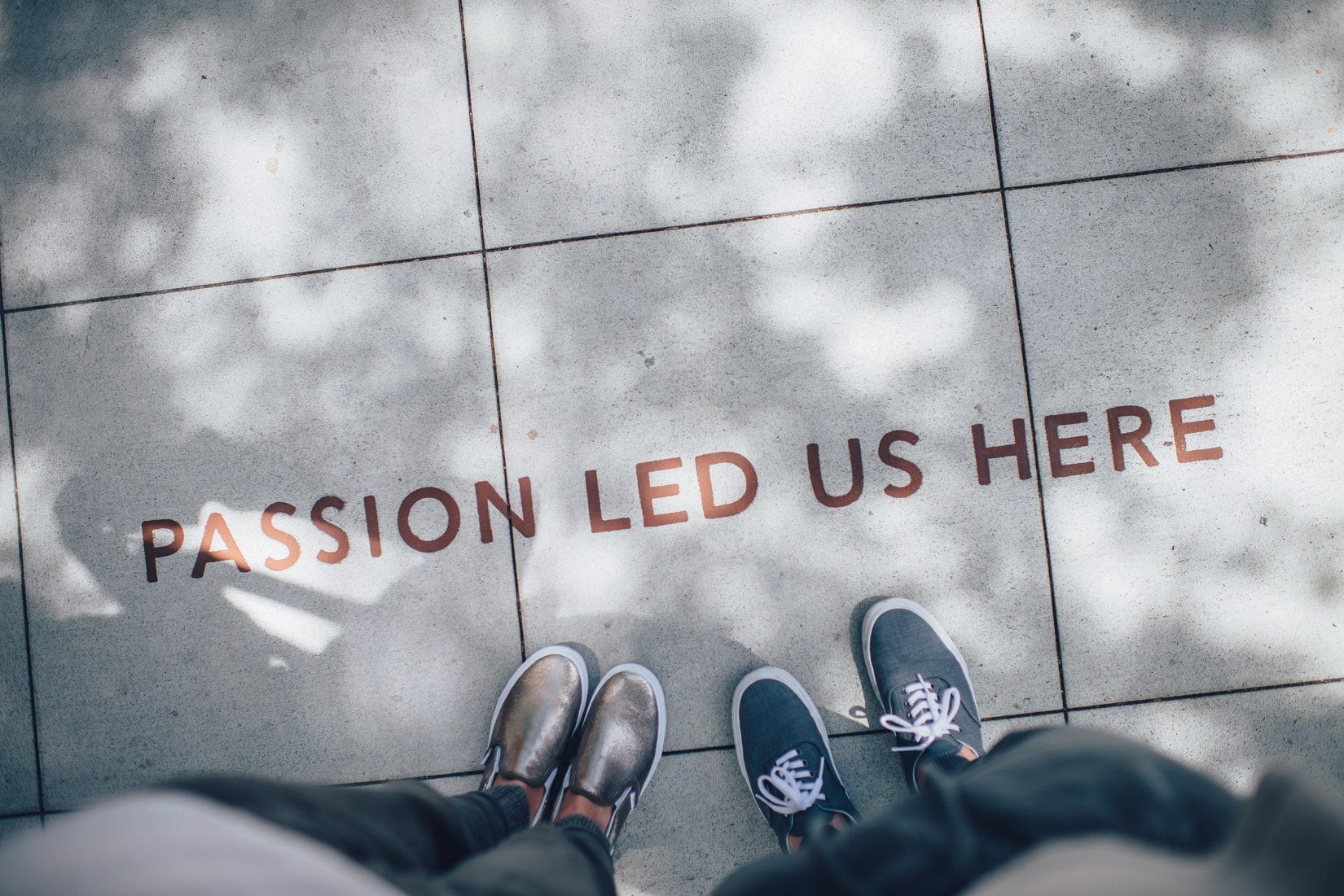 Two people’s feet standing near a sidewalk that says “Passion led us here”