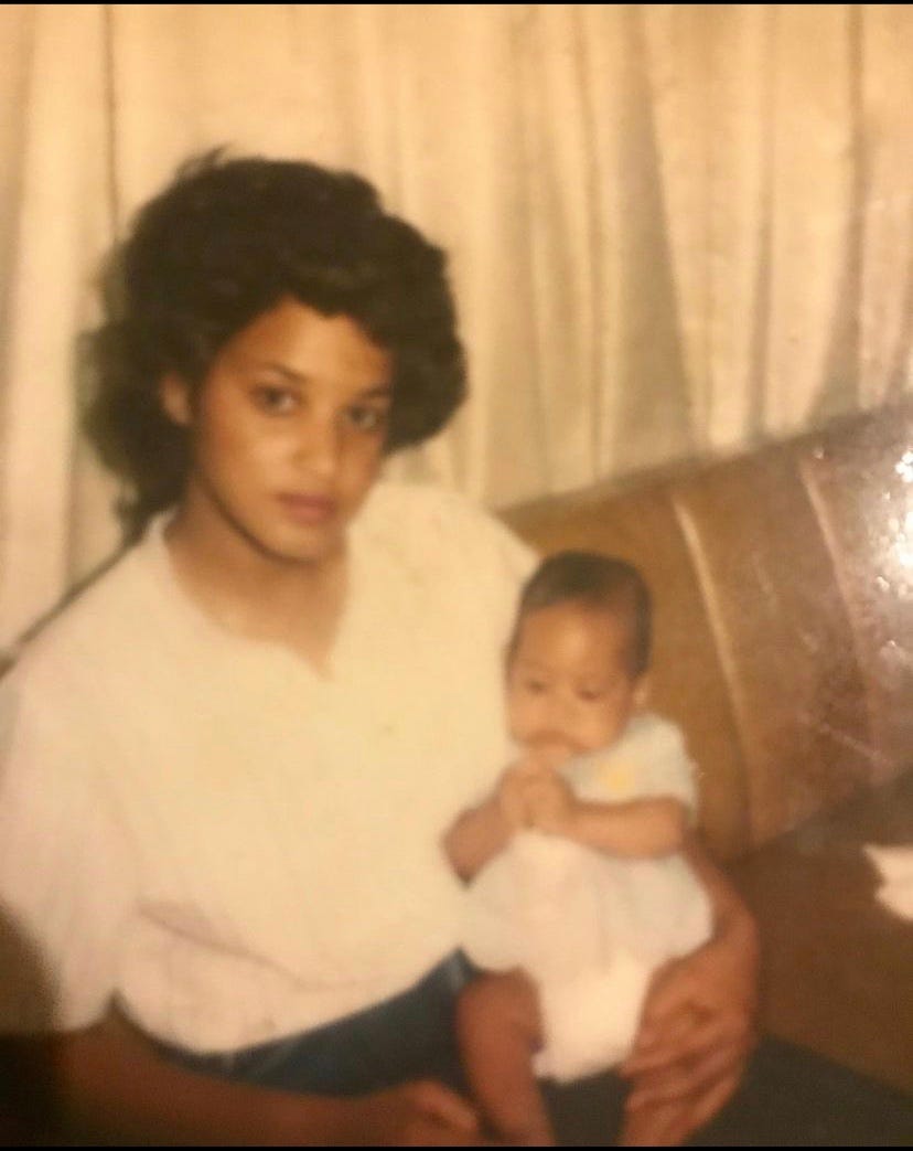 A sepia toned photo of a beautiful Black woman with light brown skin and voluminous black hair holding a baby.