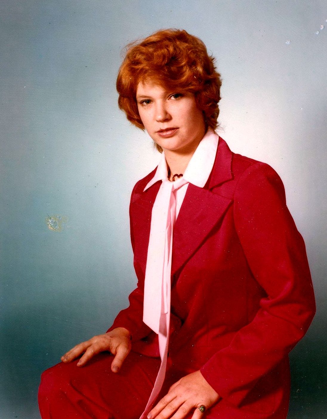 A young woman dressed in a red suit looks towards the camera.