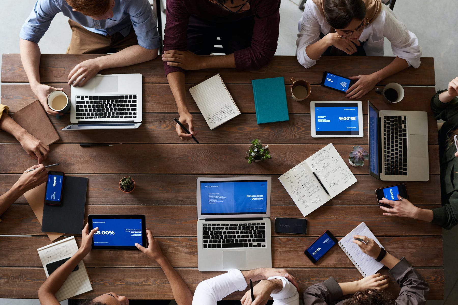 A group of people discussing over a topic on a table with laptops, tabs, mobiles and notepads.