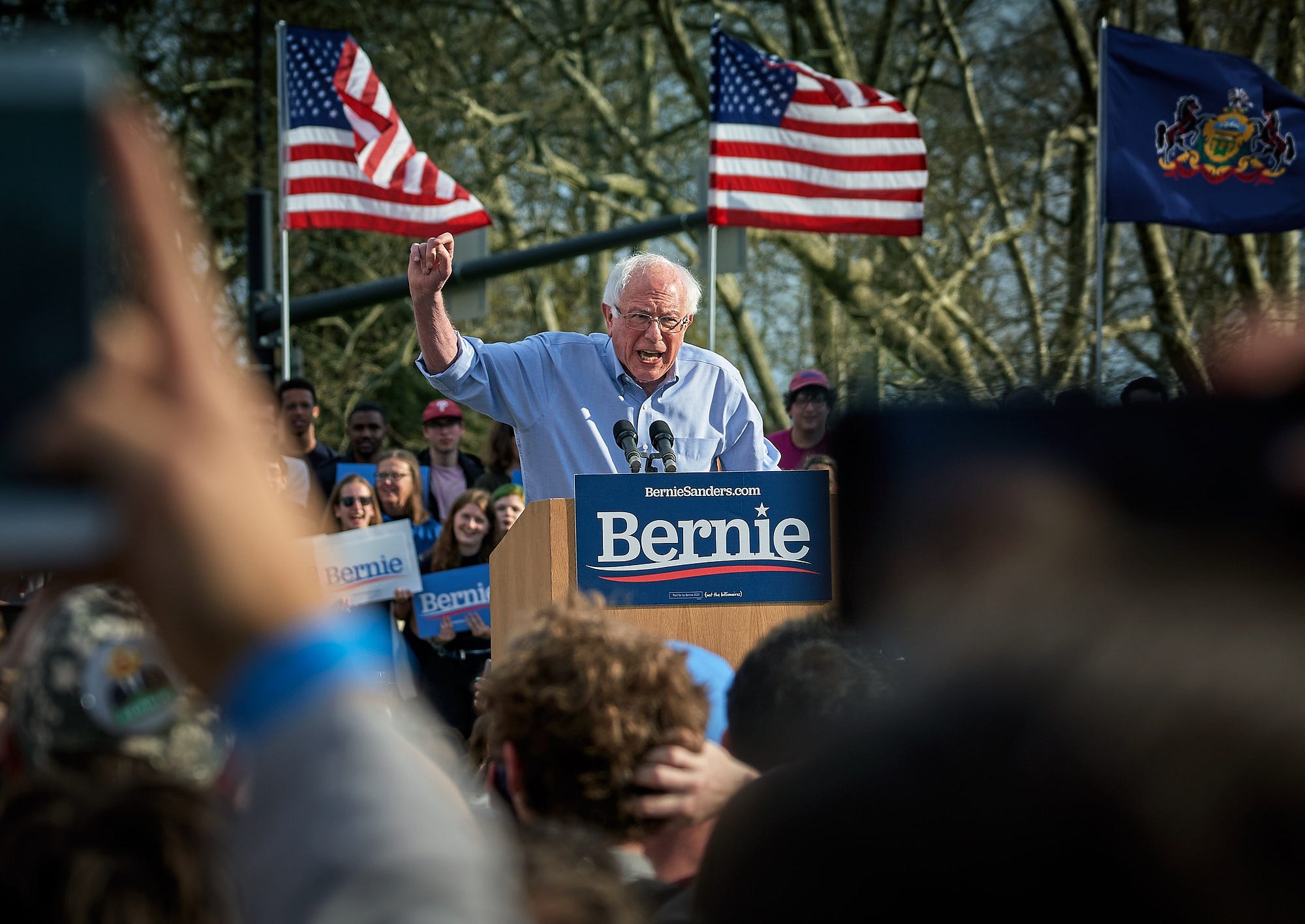 Bernie Sanders speaking at a podium outside, with American flags behind him