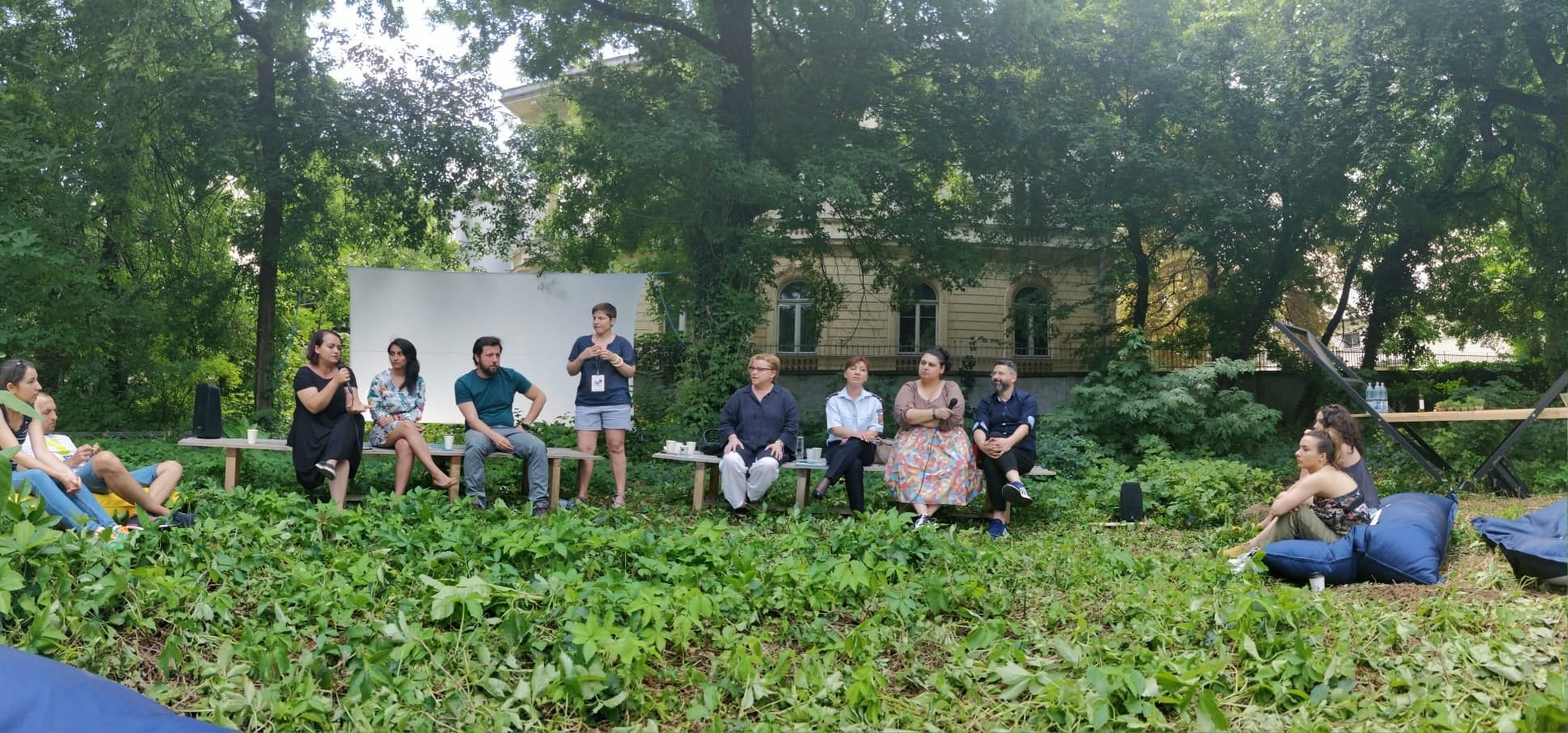 Several people meeting outdoors surrounded by plants and trees.