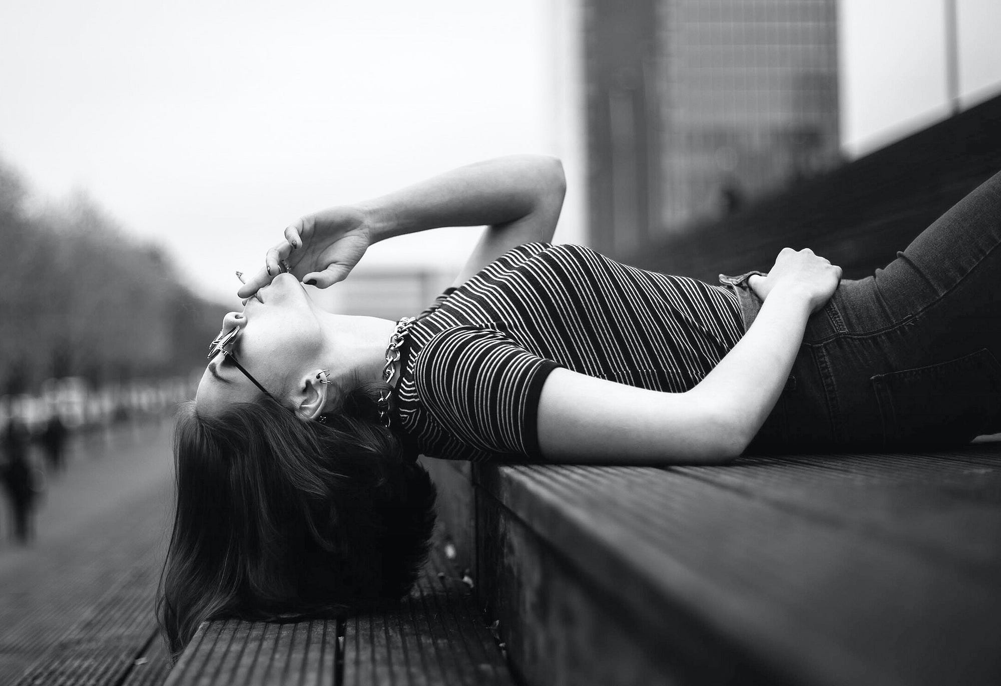 B&W photo of woman, supine on public steps smoking, looking up.