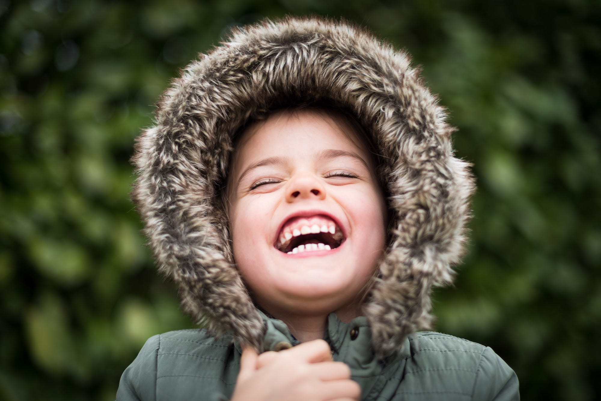 smiling child holding in jacket with fur lined hood green landscape background