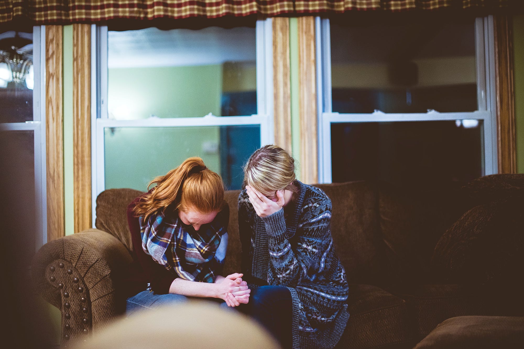 Two women sitting on a couch, crying and holding hands.