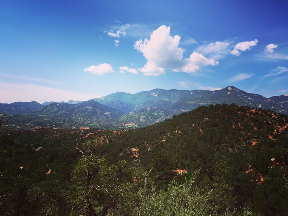Beautiful lush, green mountain range filled with trees, sitting under a deep blue, cloudy sky.