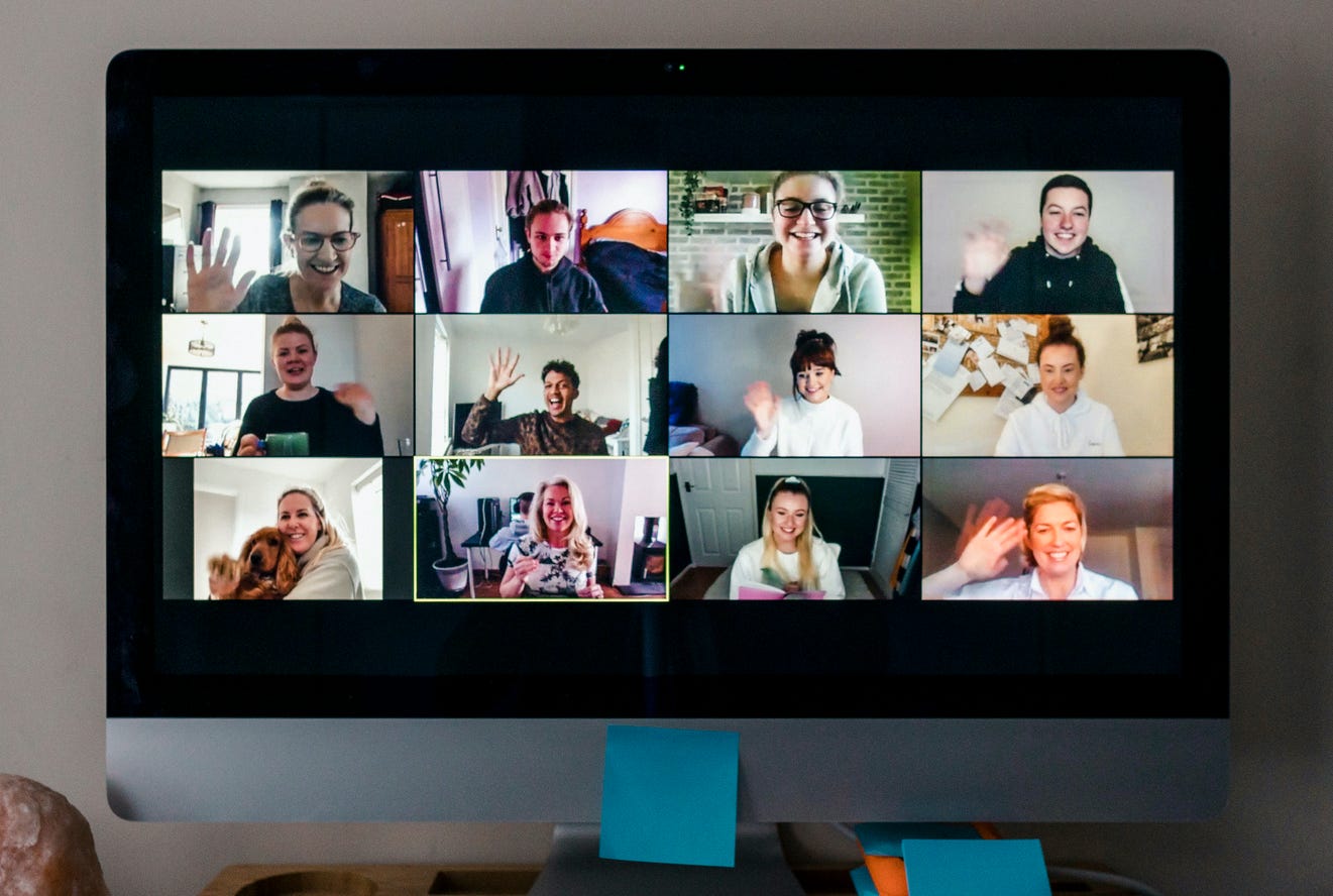 Friends waving to each other during a large video conference call on a computer screen.