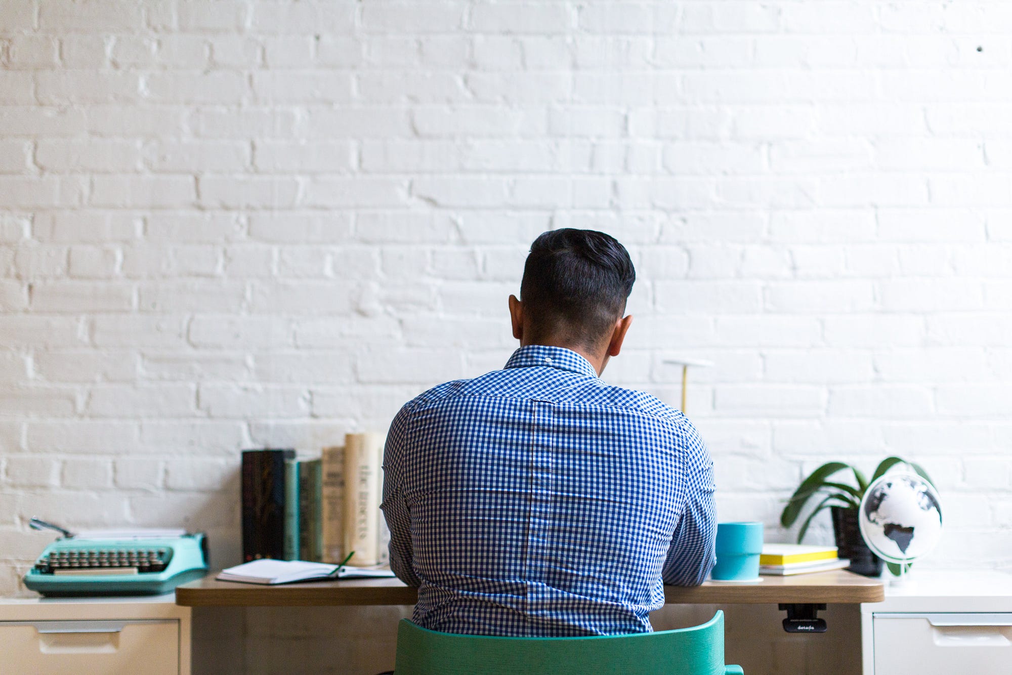 man sitting at a desk thinking and working, his back to the viewer
