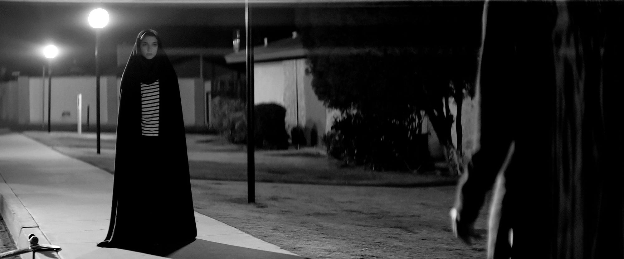 A female vampire wearing a chador stands looking at an unseen character.