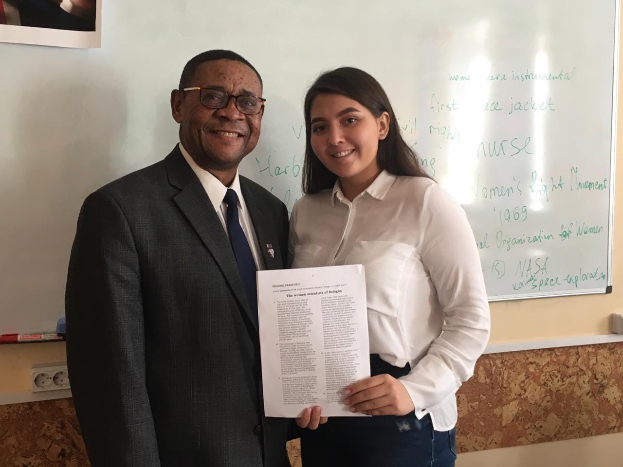 A smiling man and college-aged woman stand shoulder to shoulder in a classroom.