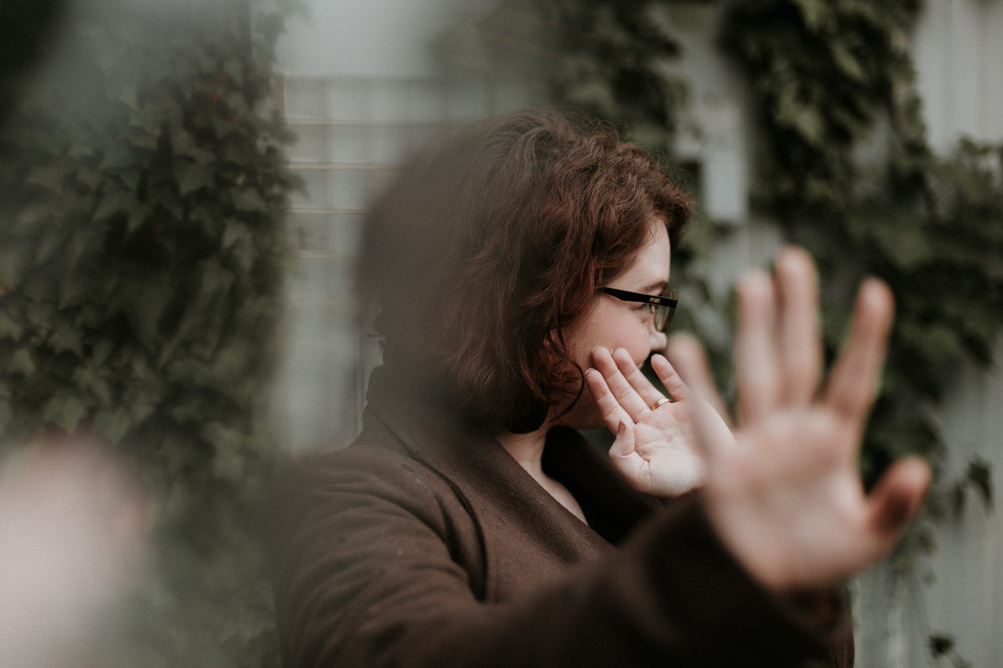 Person in brown jacket, holding hands up and away from their body in a stop, block motion