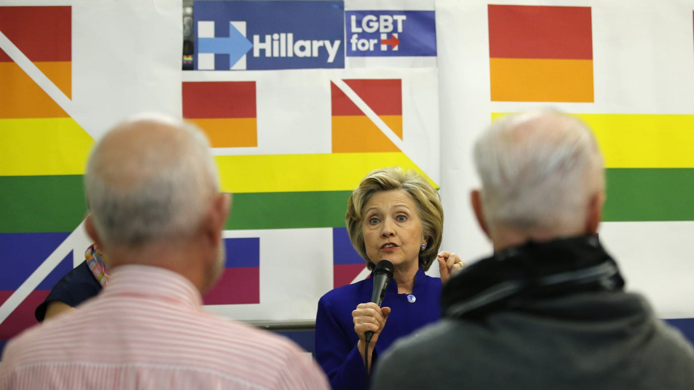 Kathy Willens/AP — Hillary Clinton using a mic, a rainbow version of her campaign logo behind her