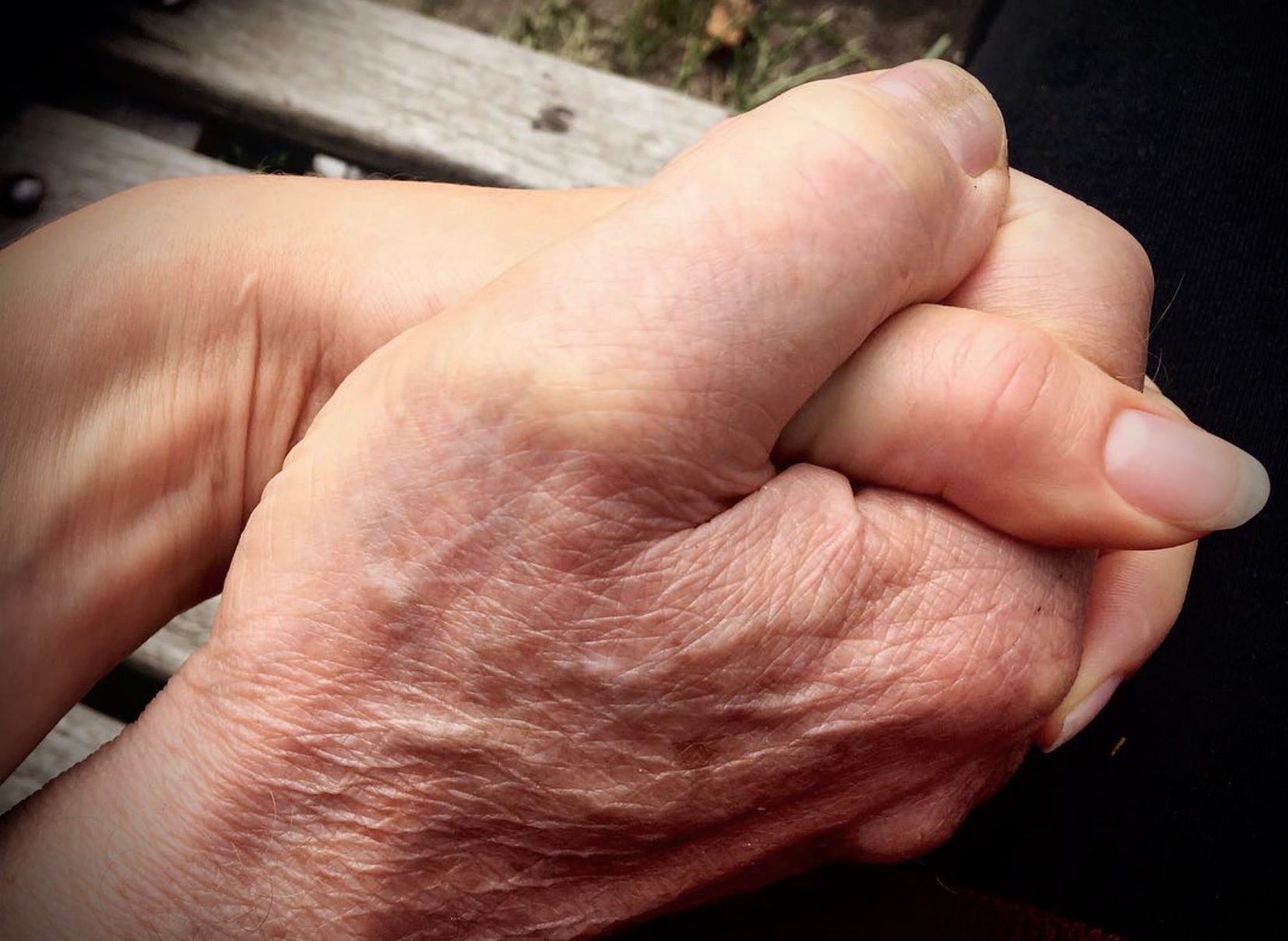 Young woman’s hand holding her father’s bigger, ageing hand