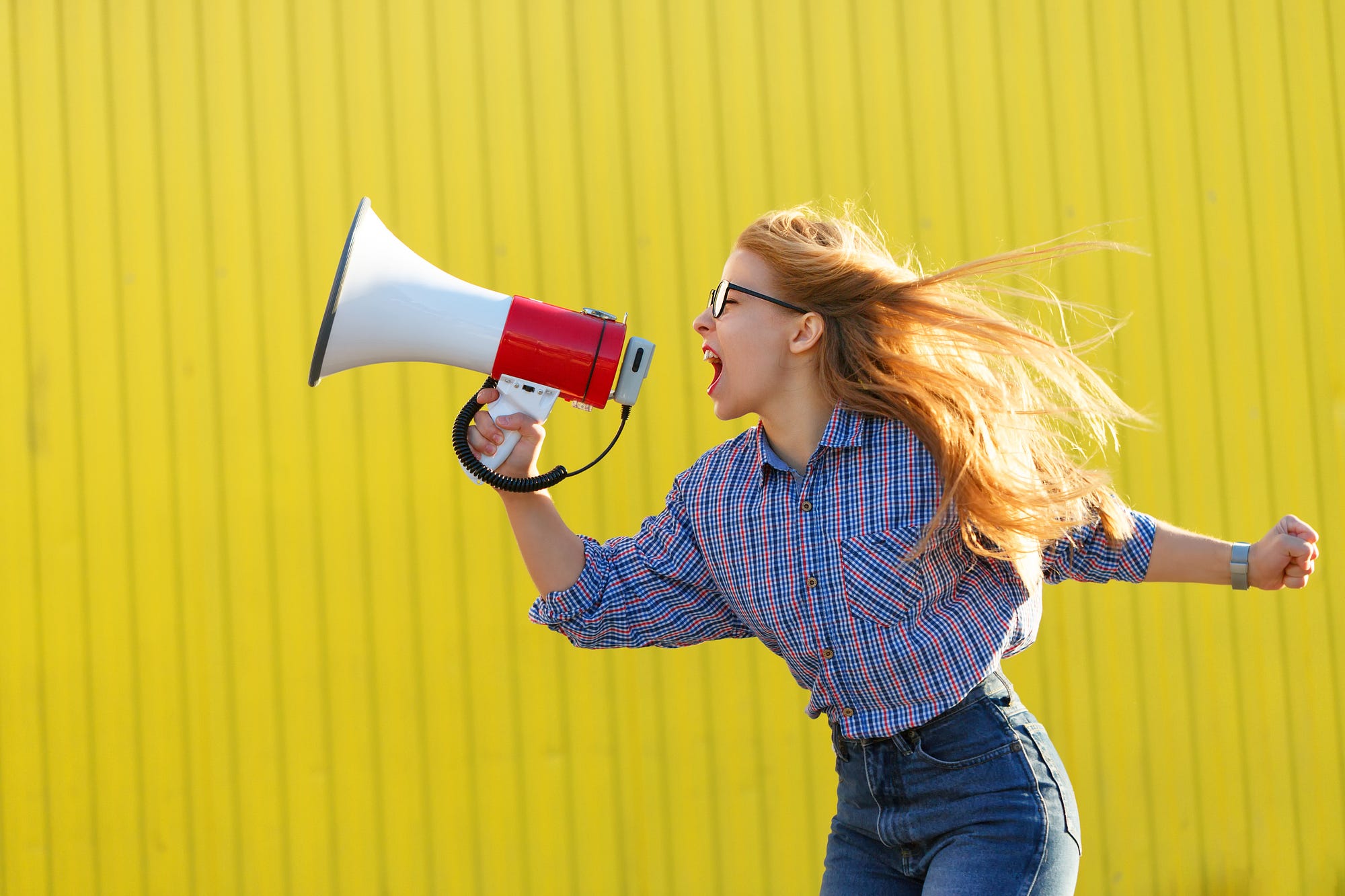 A person with long hair screaming into a megaphone.