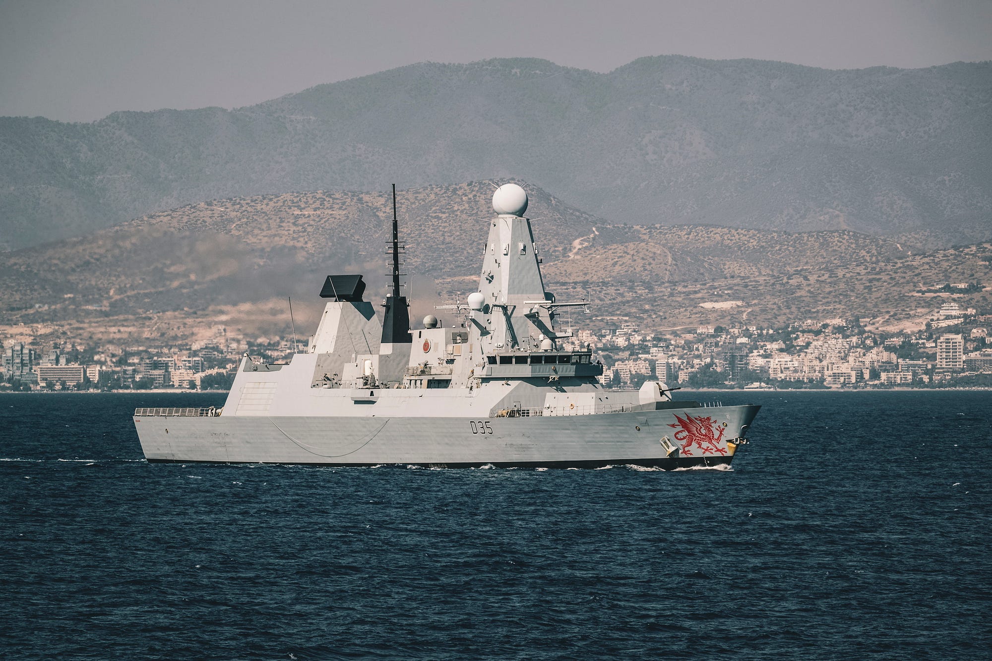 A warship at sea, with a coast in the background