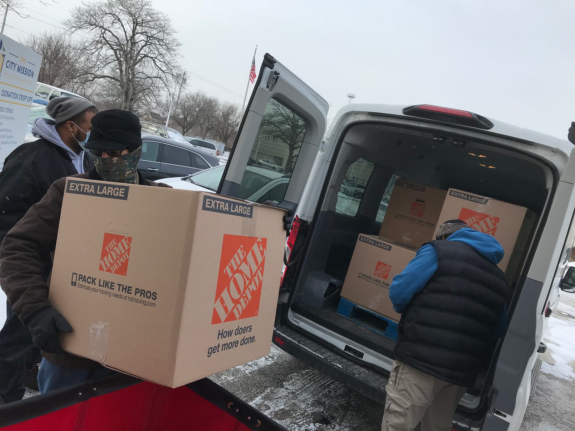 two men bundled in winter coats empty large boxes from the back of a delivery van as a Sewer District employee delivers donations on a cold February morning.