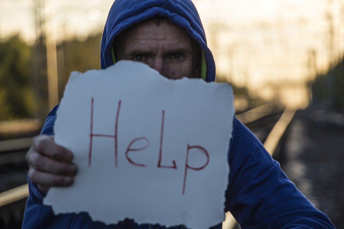 Mann mit Kapuze hält ein Schild auf dem Help steht.