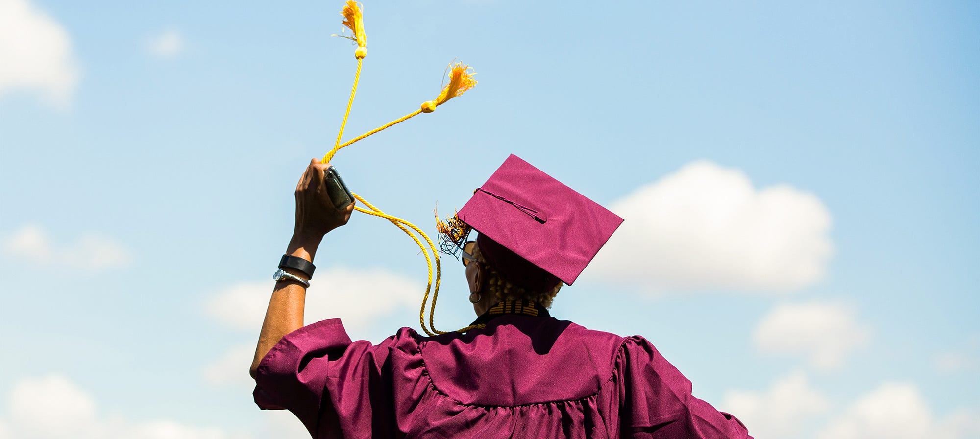 Arizona State University graduate wearing maroon cap and gown, twirling gold tassels in left hand.