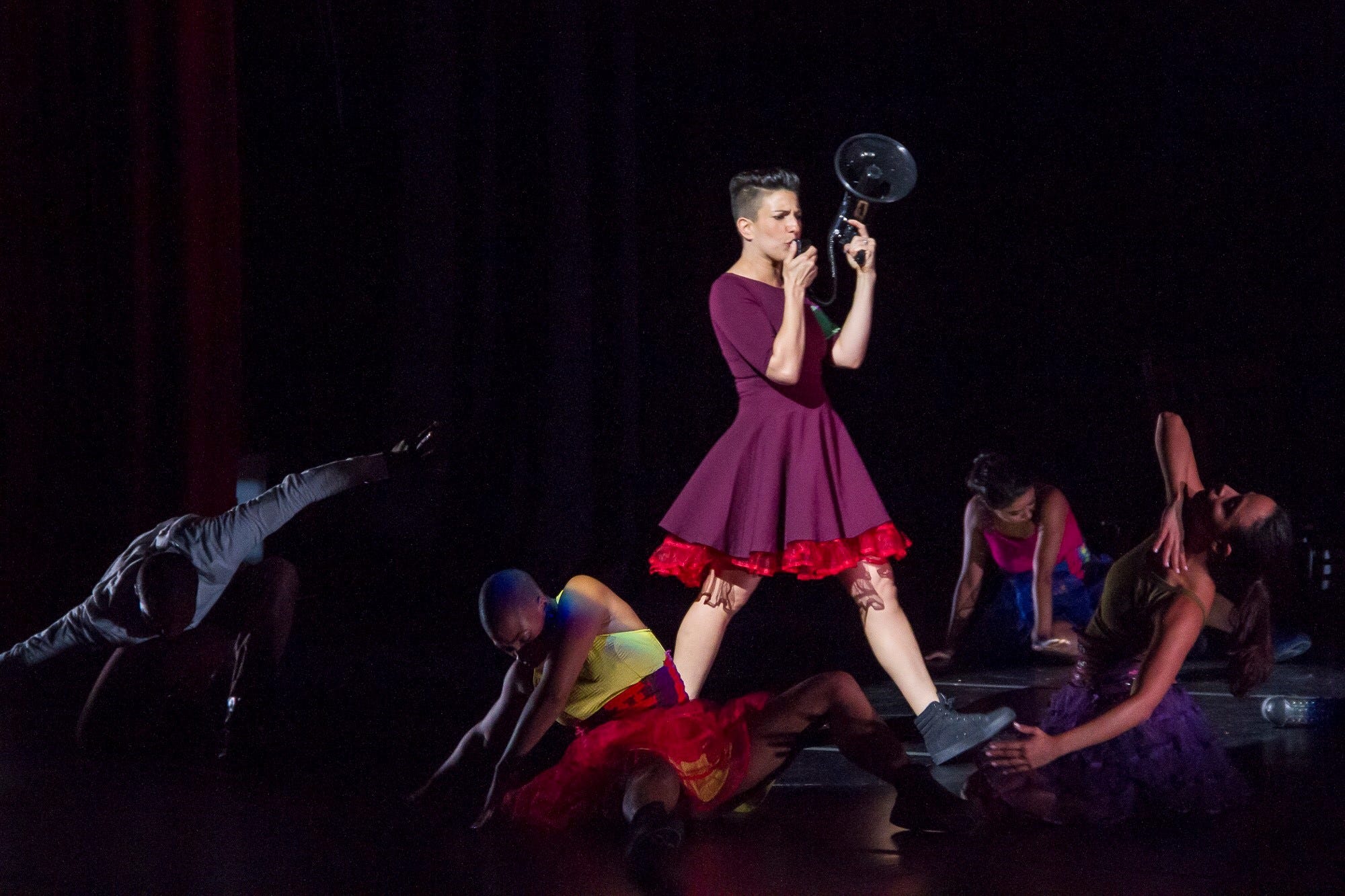 Woman in dress walking through group of performers holding a megaphone