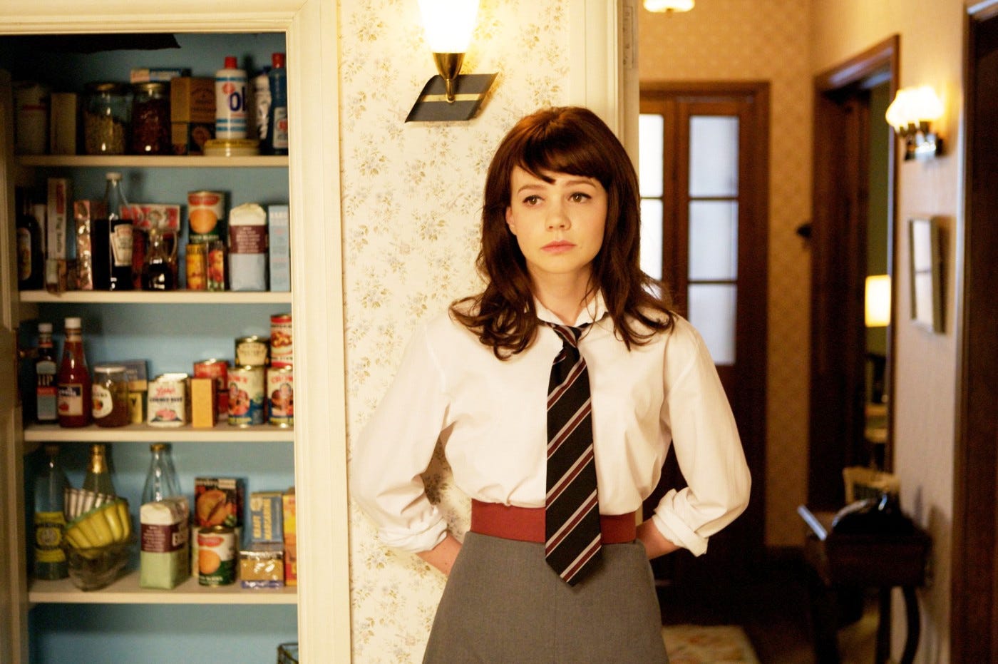 Carey Mulligan in a school uniform standing near a larder and looking pensive