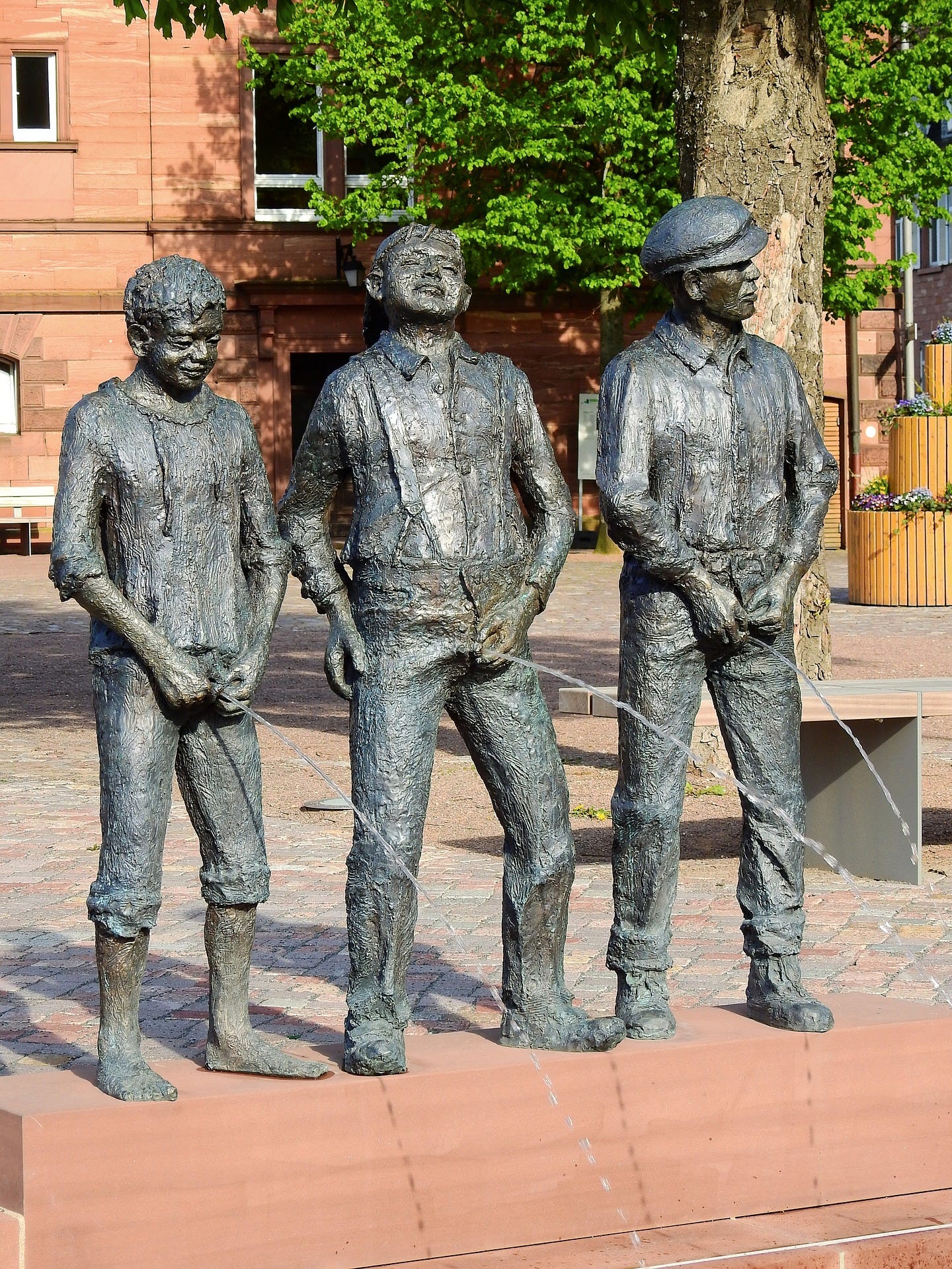 An odd sidewalk fountain depicting three young men in old-fashioned clothing, lined up, taking a piss. Each has a different facial expression.