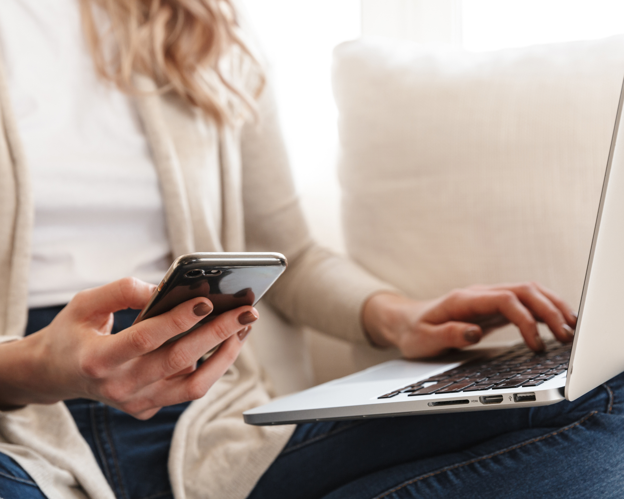 Woman typing on laptop and holding smartphone