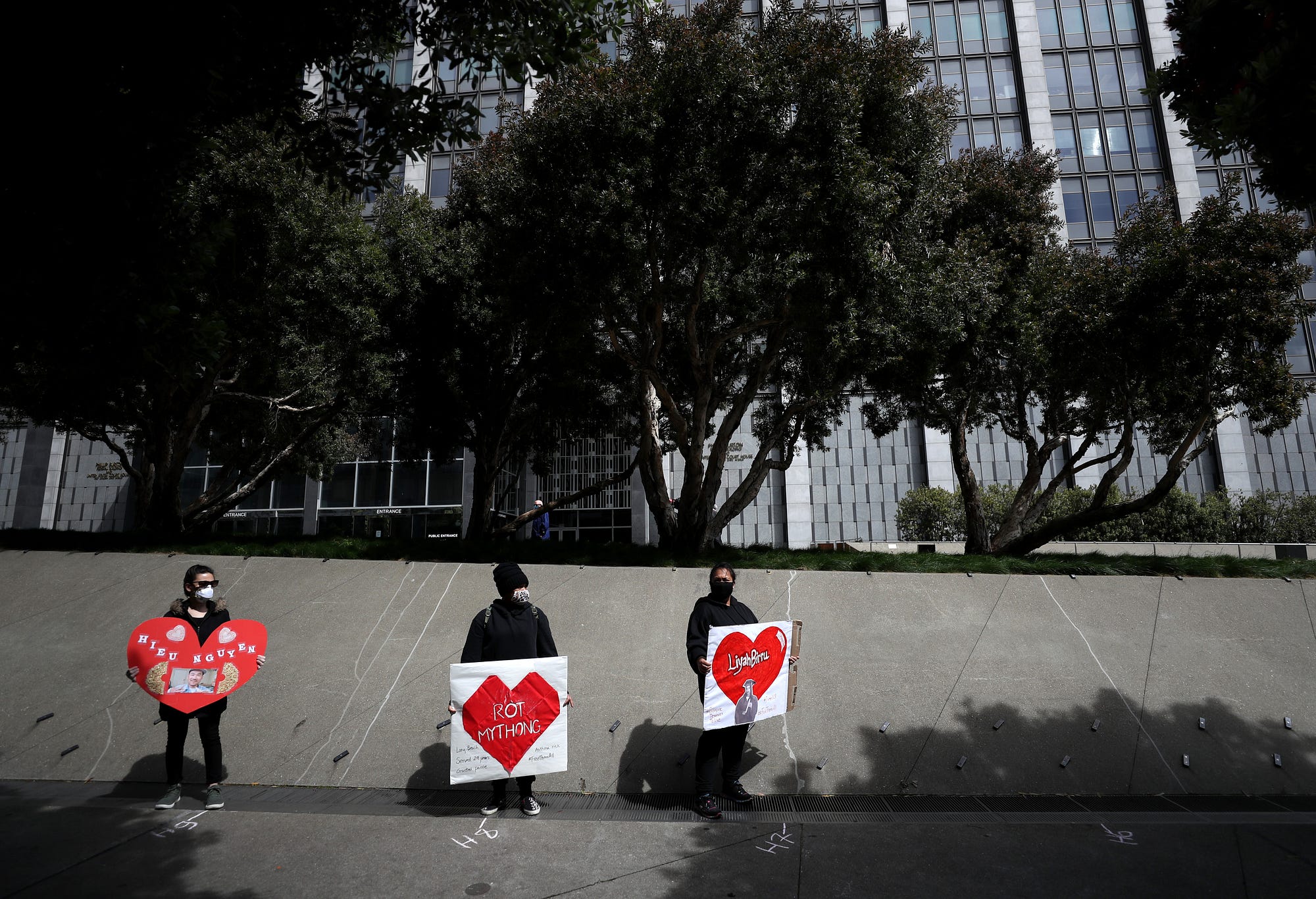 Activists hold signs and tombstone shapes in front of the Phillip Burton Federal Building to honor Covid-19 victims.