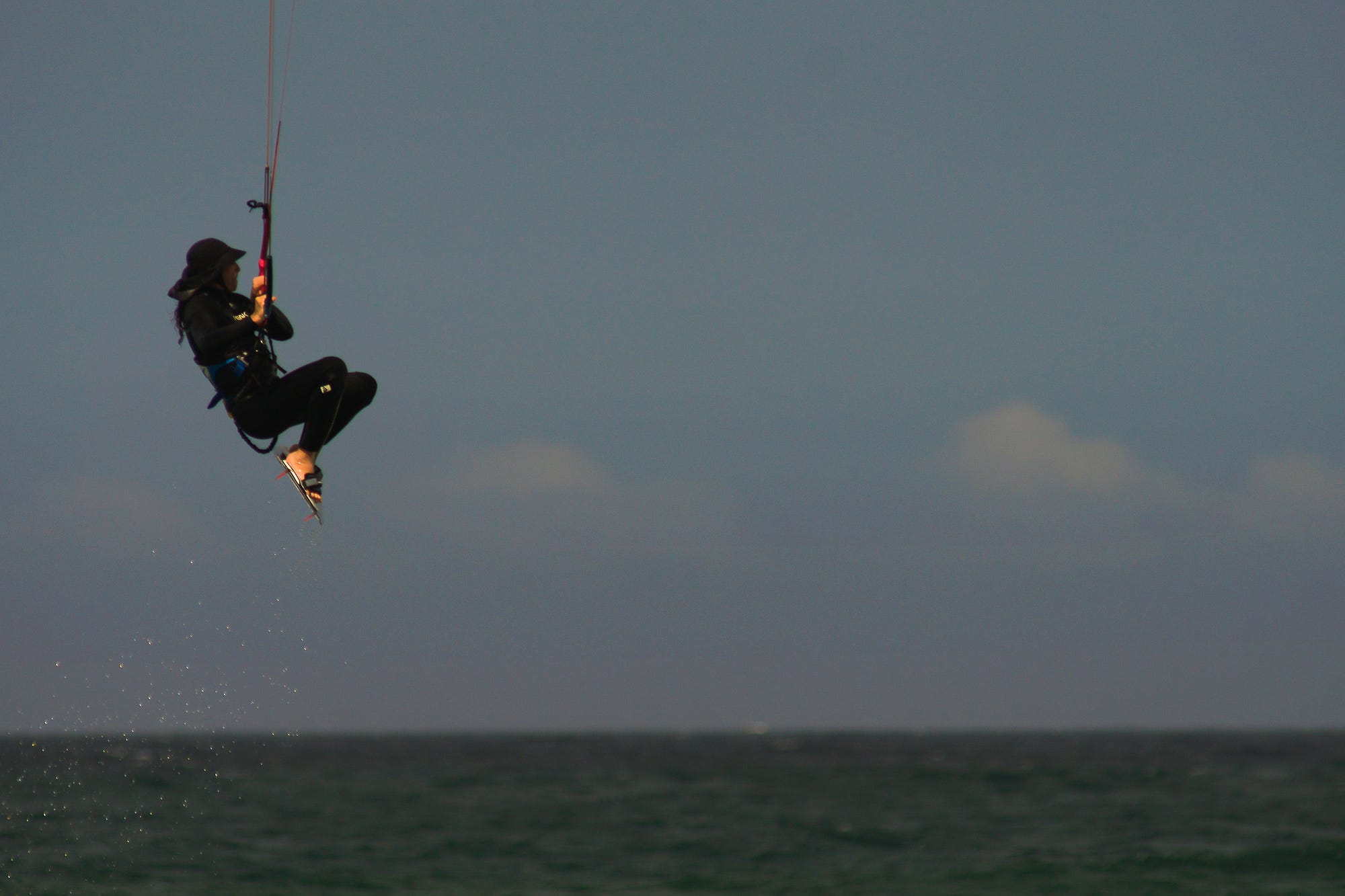 An image of Uzi windsurfing — you can’t see the parachute, just the sky, the ocean and Uzi dangling from a harness in mid-air.
