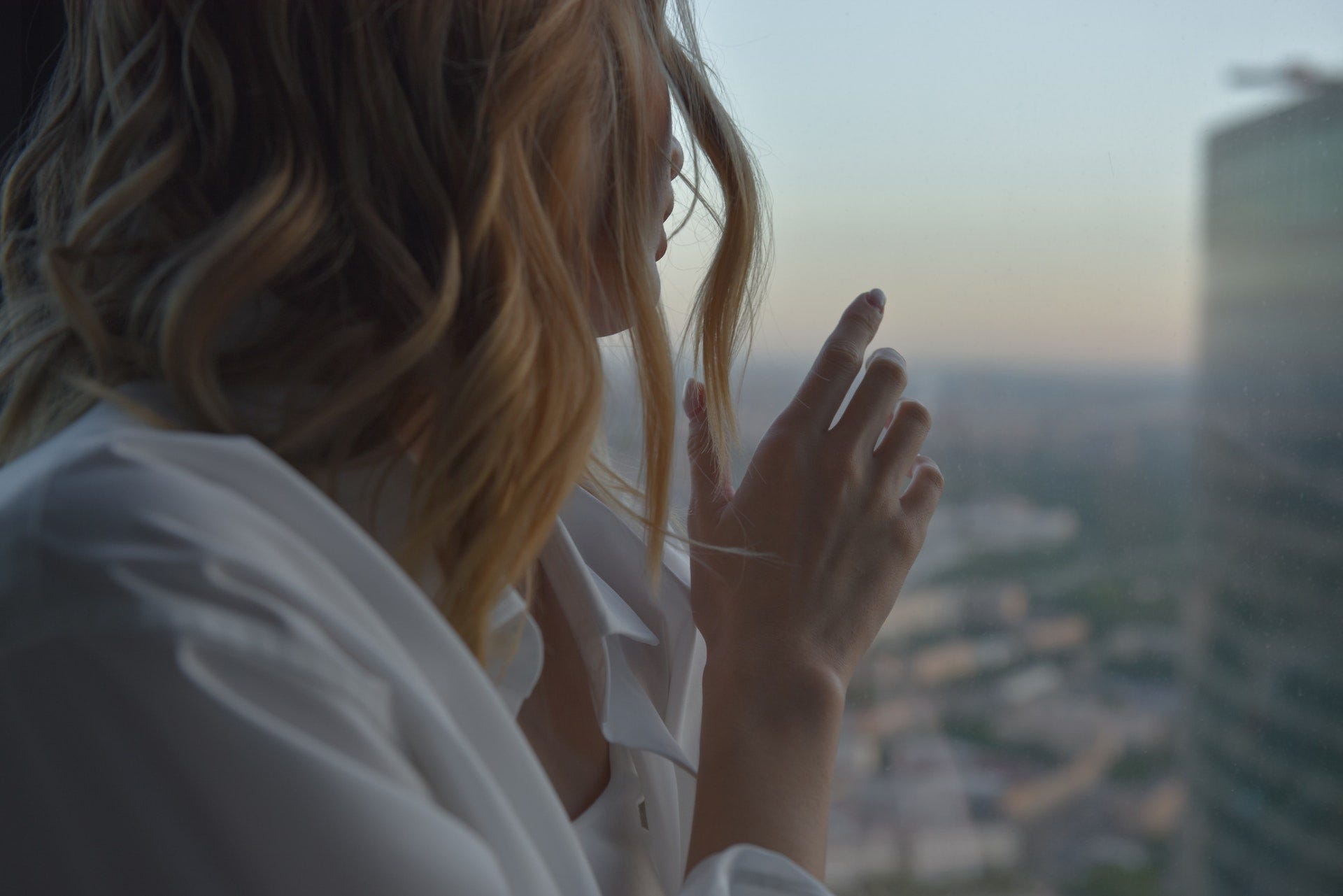 Woman in white shirt looking out of a high rise building window