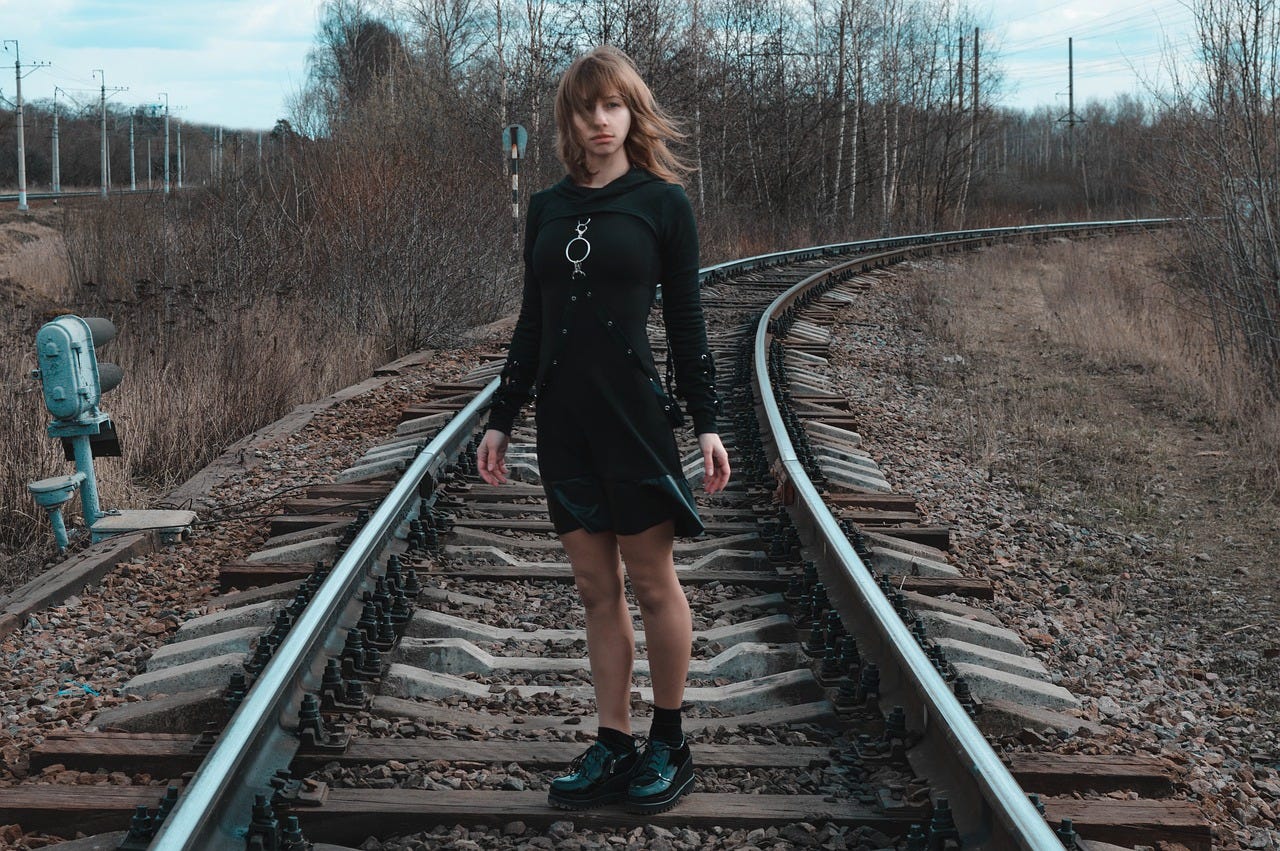 A young woman dressed in black, standing on a railway line.