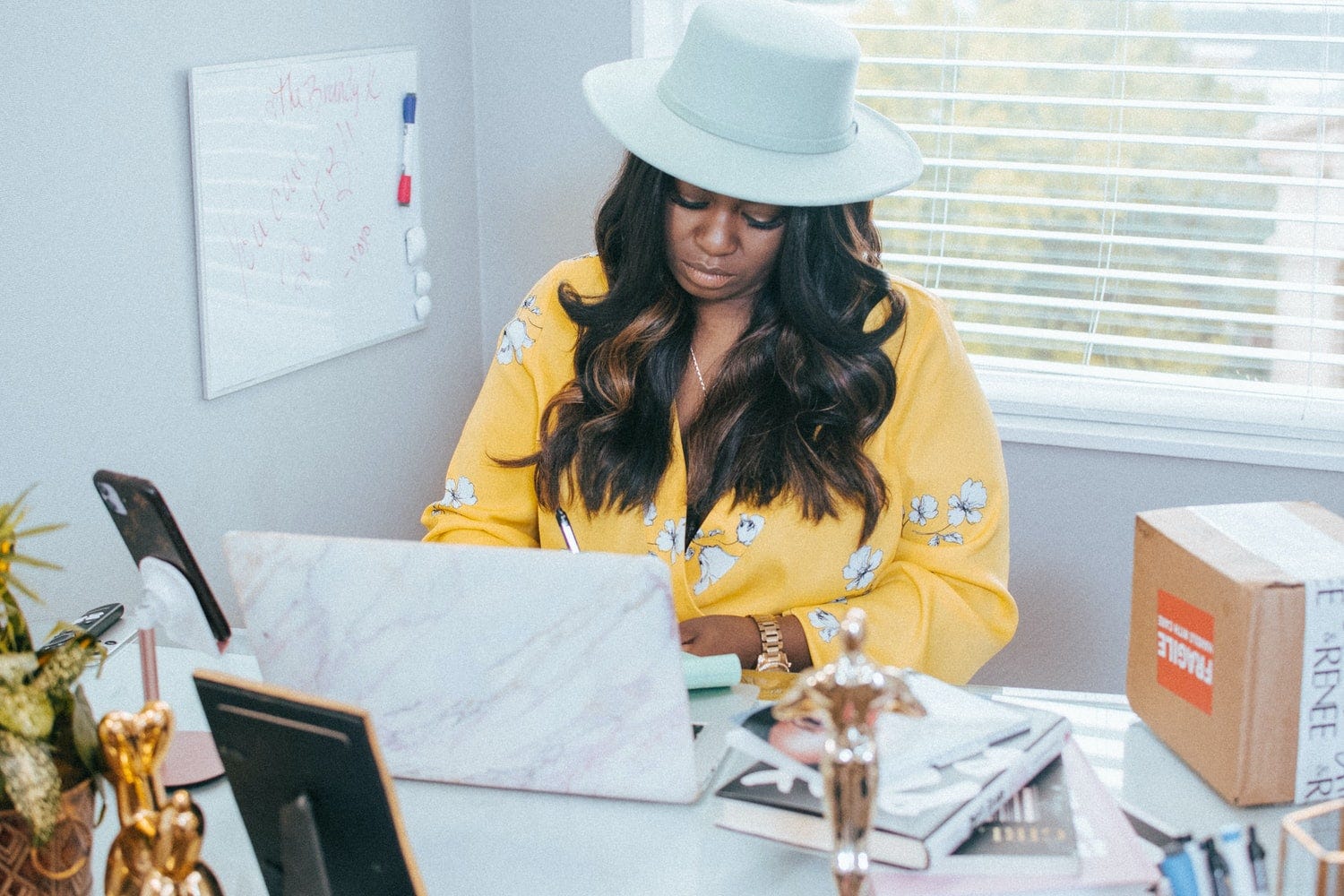Woman wearing a hat writing at a laptop.