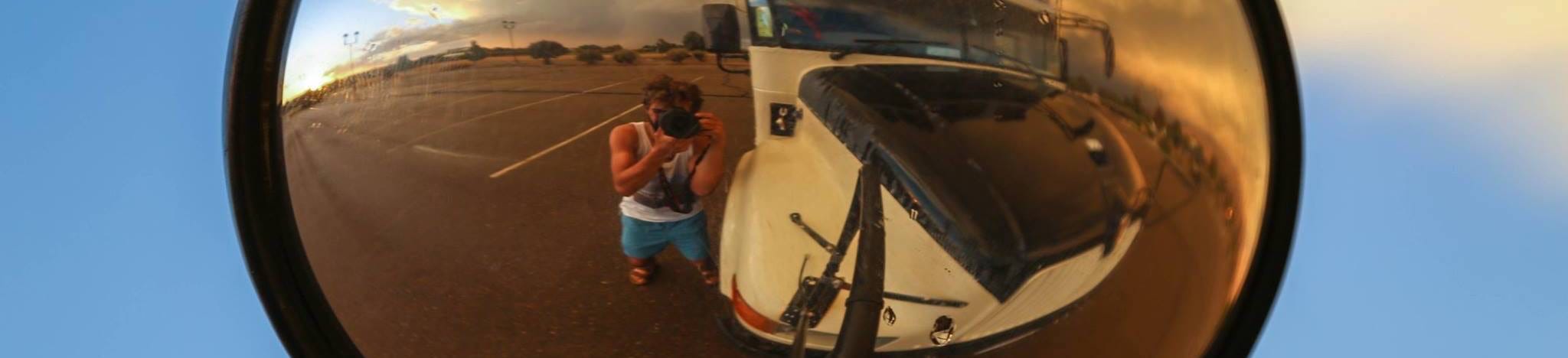 man taking photo of himself using the side mirror of a school bus