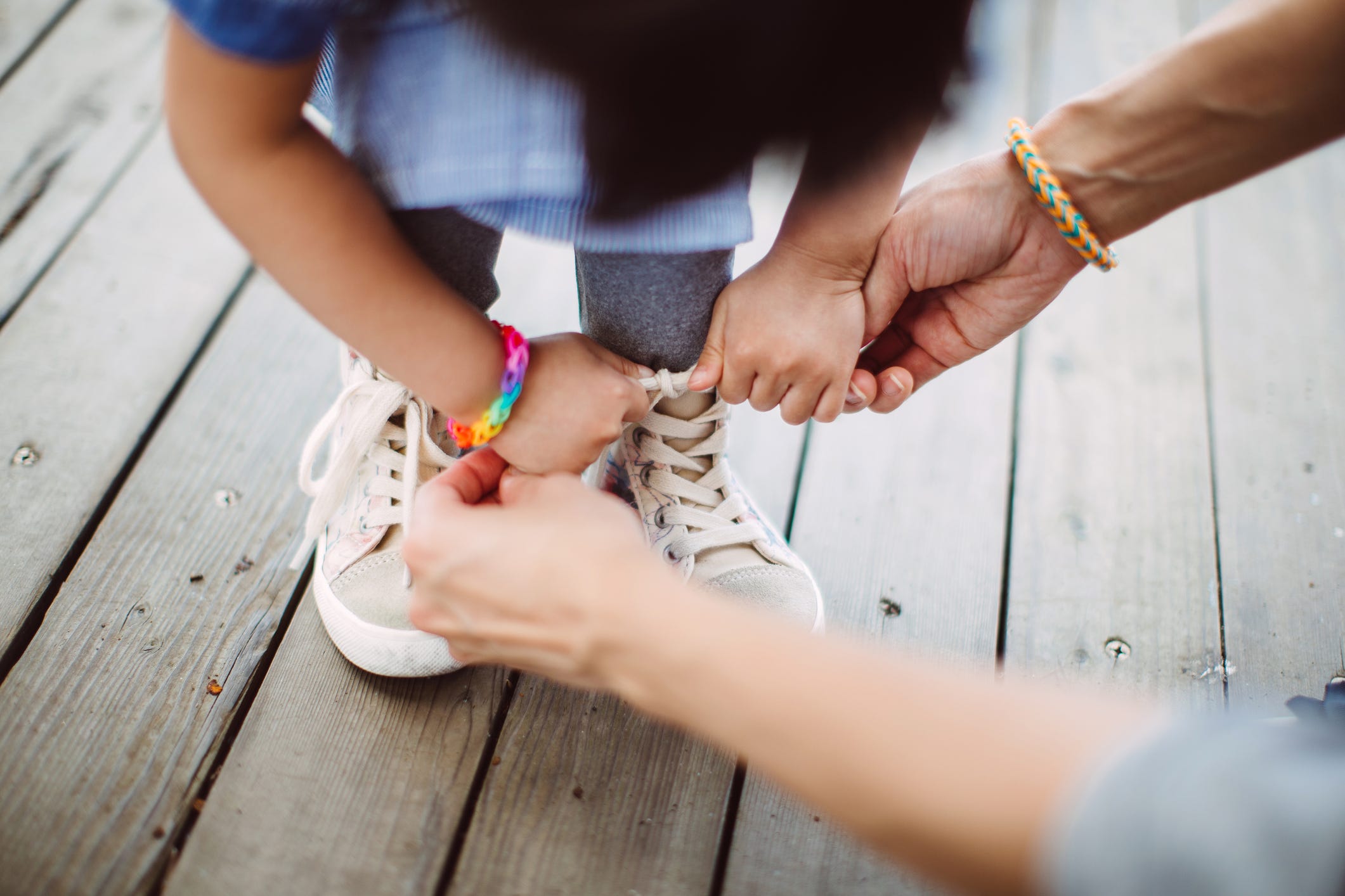 A parent helps a child tie their shoelaces.