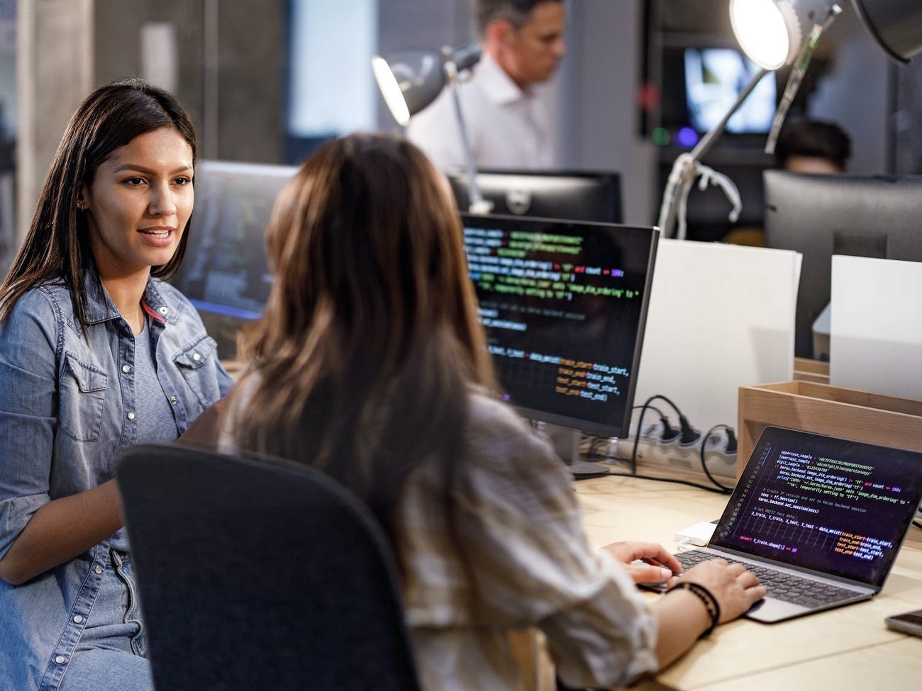 Two women talking to one another and on computers.