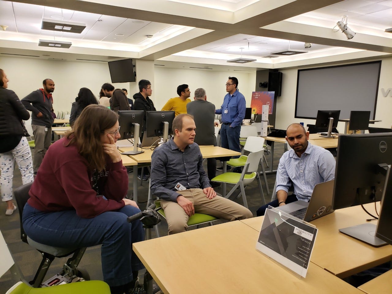 A group of people watching a demo with other participants chatting in the background