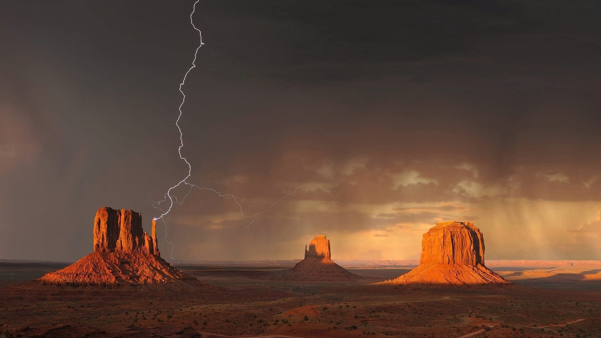 Three formations in Monument Valley Arizona. This one has a bolt of lightning touching the point of a formation