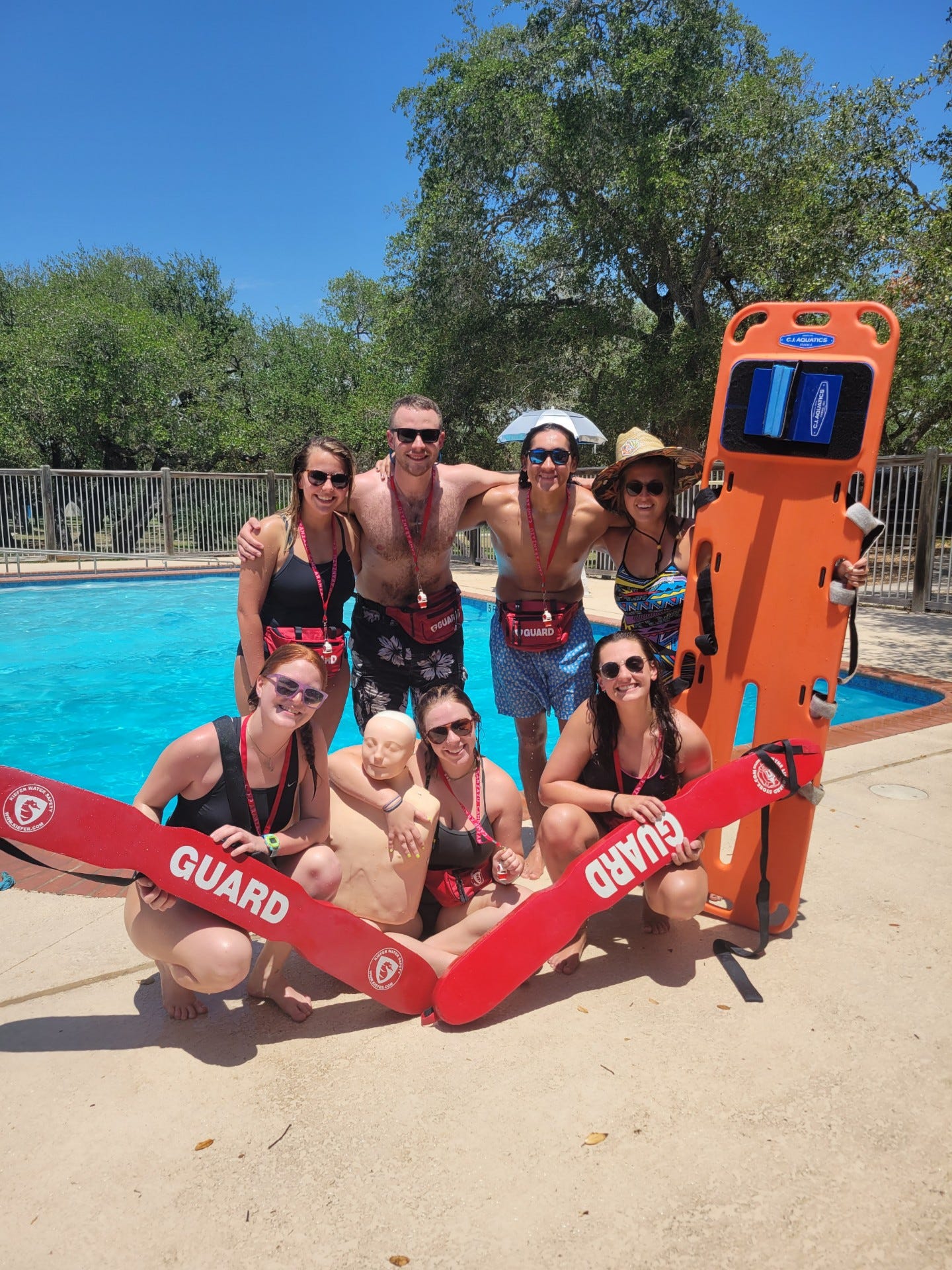 Activity leaders pose and Amelia pose with lifeguarding supplies in front of the party pool after a long week of training
