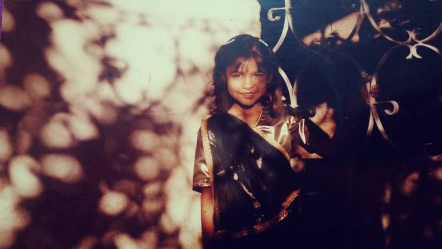The author’s photograph as a child wearing a gold and green dress in the sunlight.