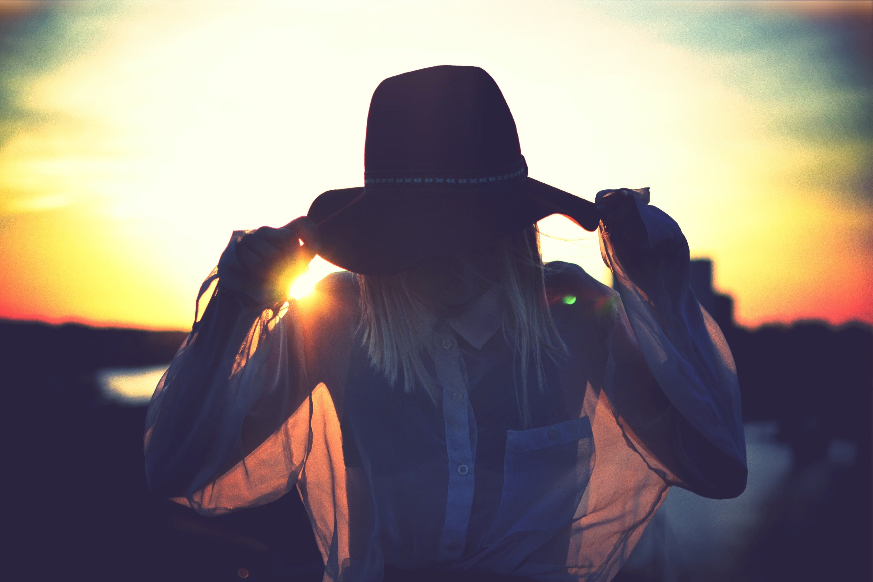 Woman with hat covering her face in front of sunset