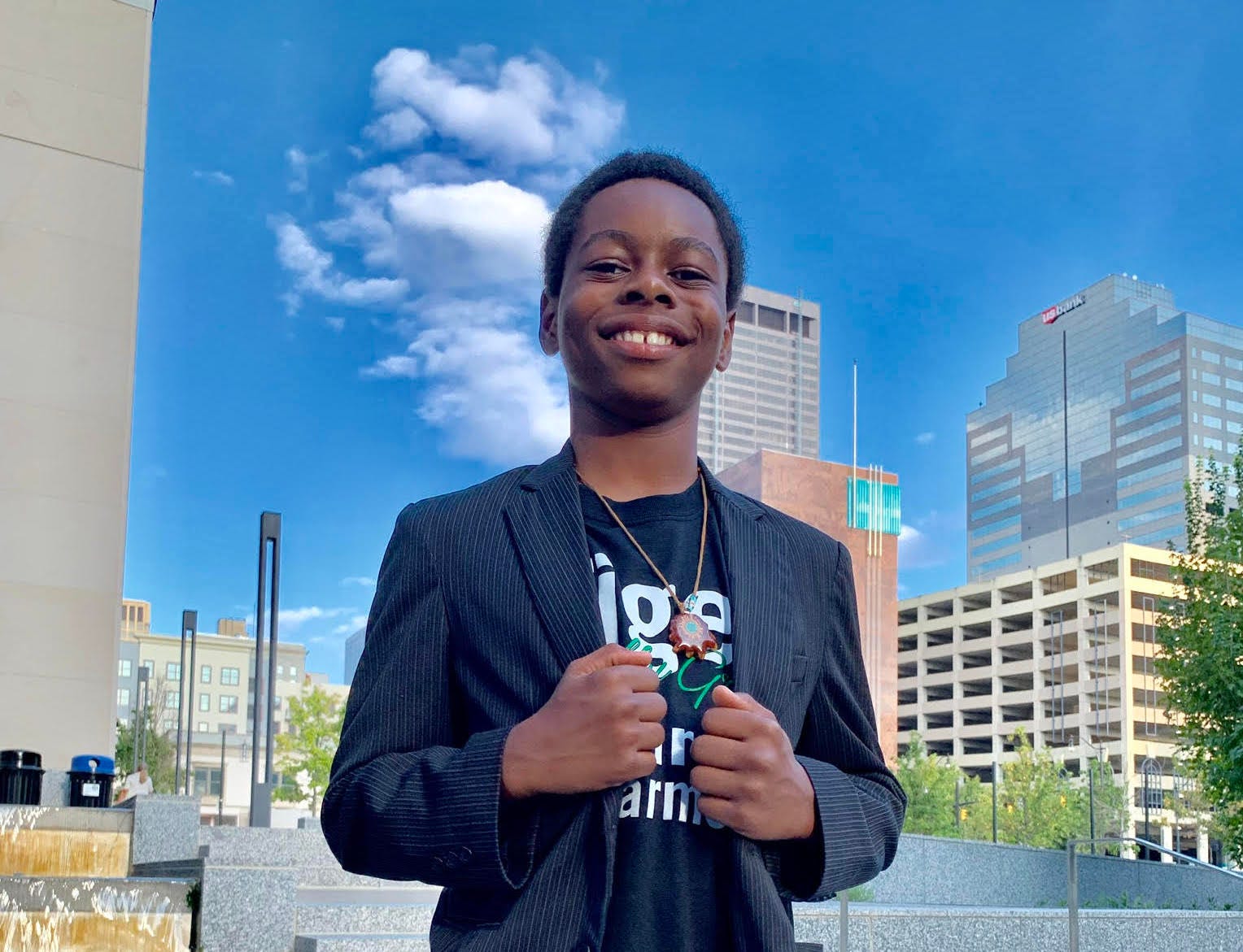 Te’Lario Watkins II smiling and posing in front of tall buildings and a bright blue sky.
