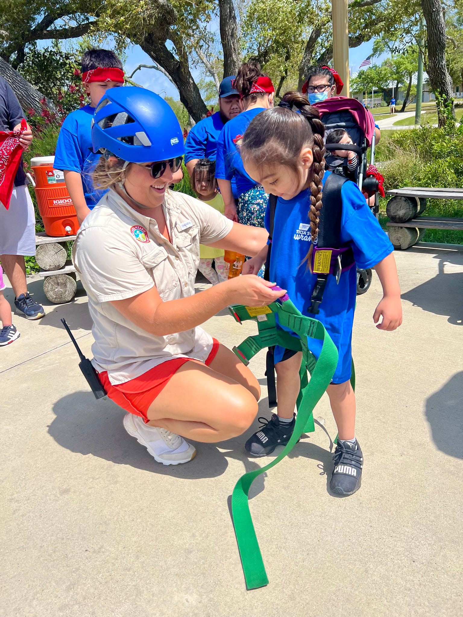 Camp Director, Amelia, prepares a small camper for rock climbing and the zipline